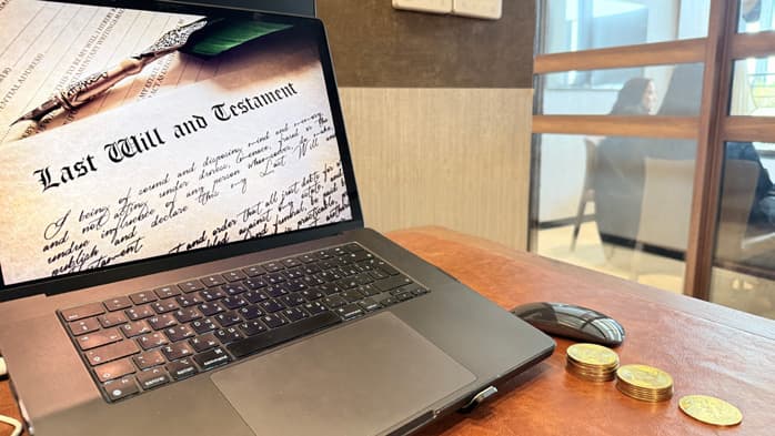 A laptop showing a Last Will and Testament document, with gold coins beside it